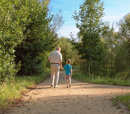 Grandfather & grandson walking on dirt path in the woods