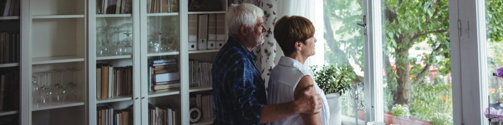 Senior couple looking through window in living room