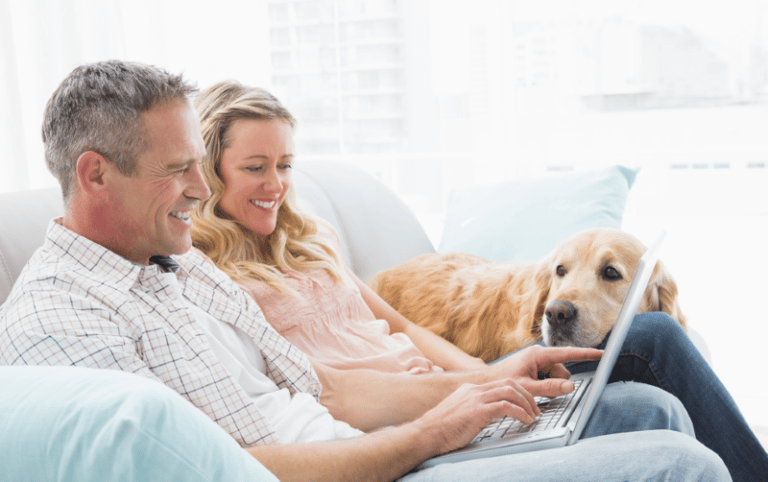 Couple sitting on couch looking at laptop with Gold Retriver