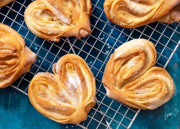 Homemade sugar buns on a cooling rack with sugar for sprinkling. Palmiers, elephant ear, puff pastry cookie.