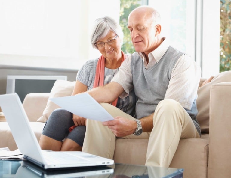 Senior man and woman with laptop reading a document at their house