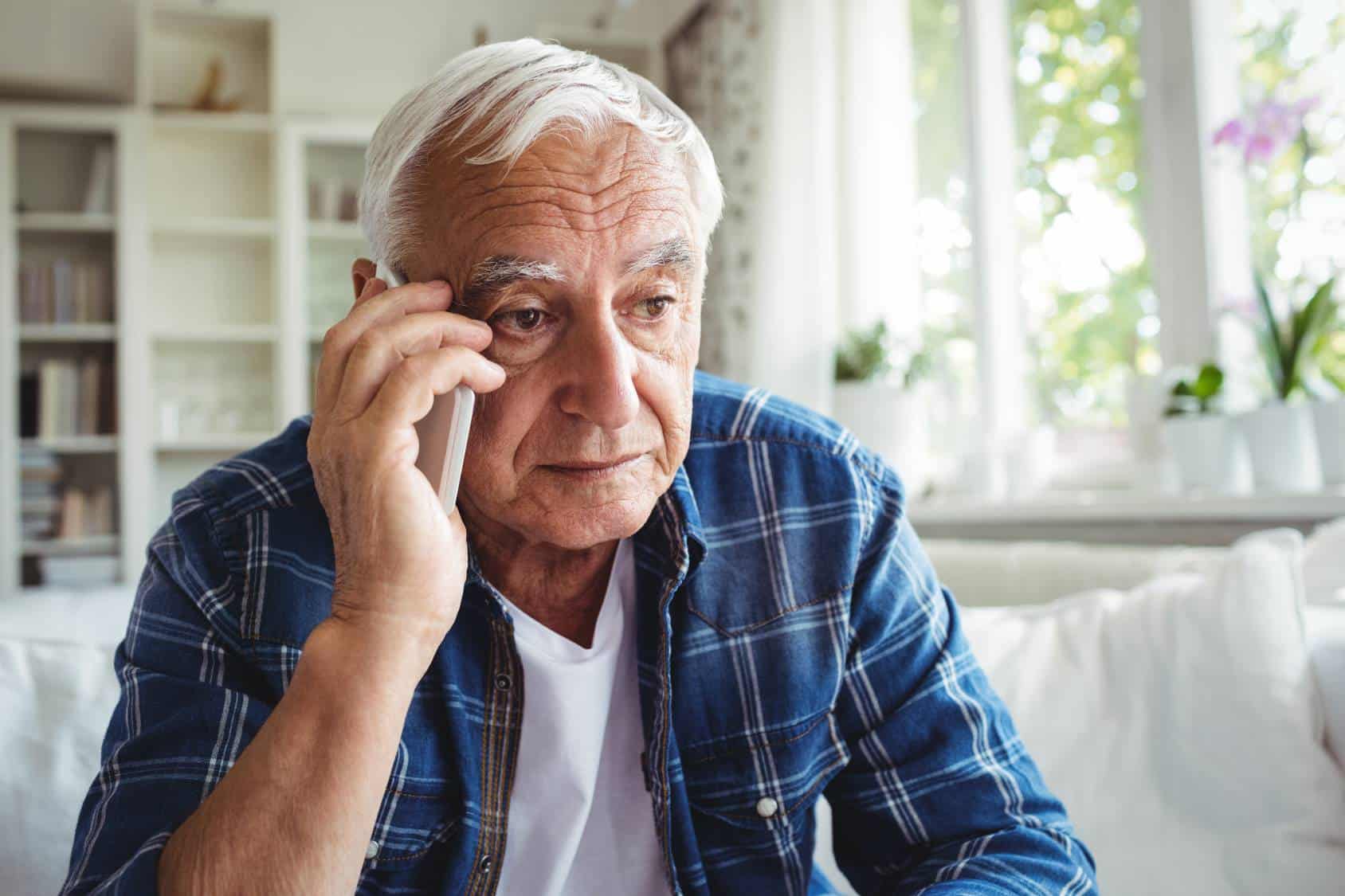Close up of tensed senior man talking on mobile phone at home