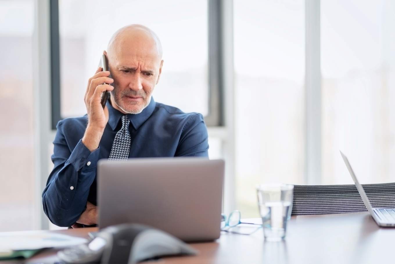 Concerned Man on Mobile Phone looking at Laptop Screen.